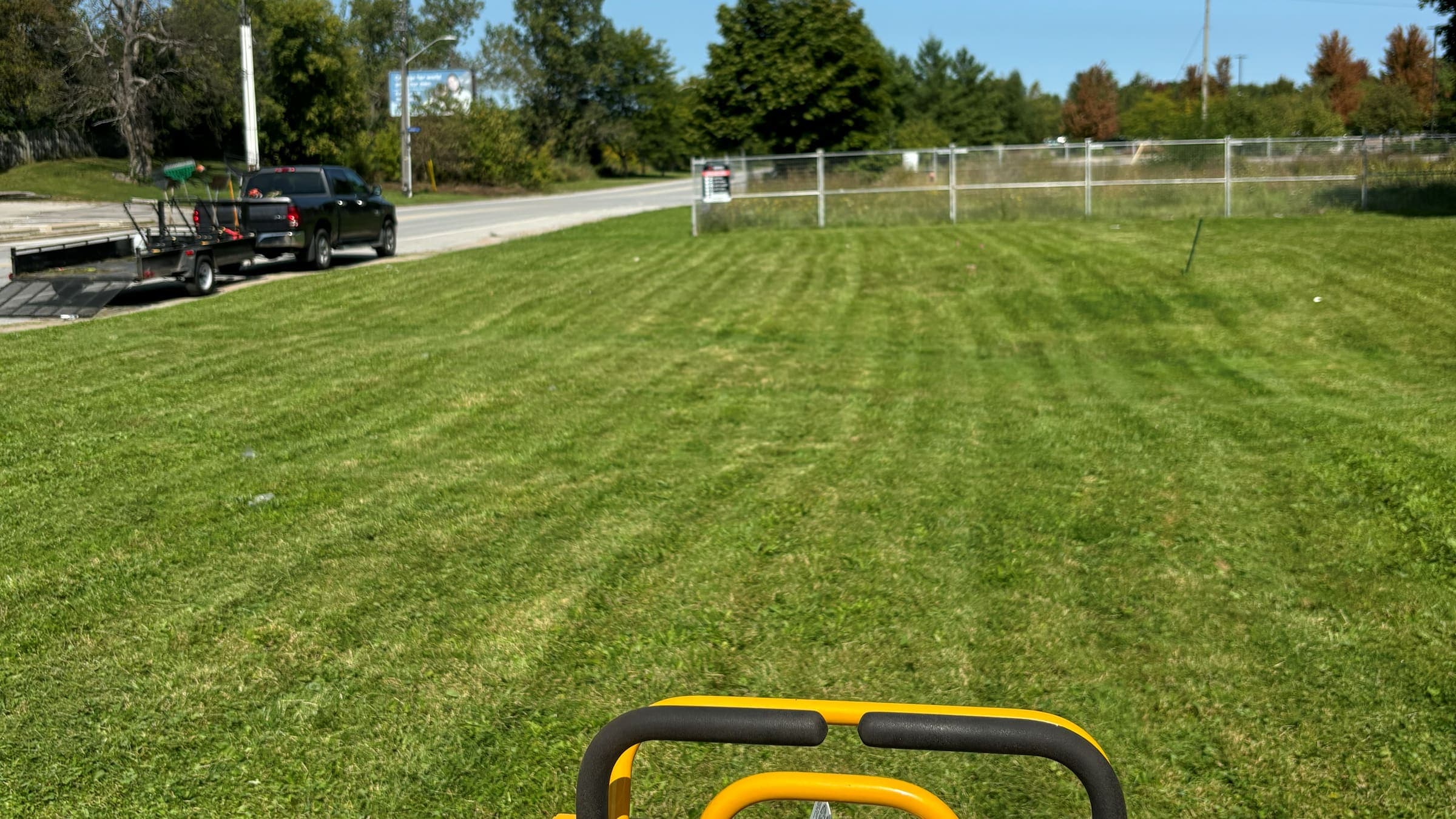 View from a stand-on mower across a freshly cut, striped lawn in Niagara Falls, with a pickup and equipment trailer parked at the roadside